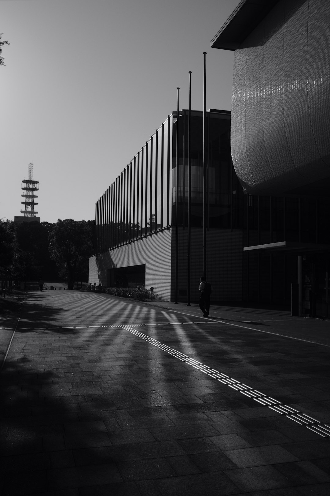 grayscale photo of man walking on sidewalk near building