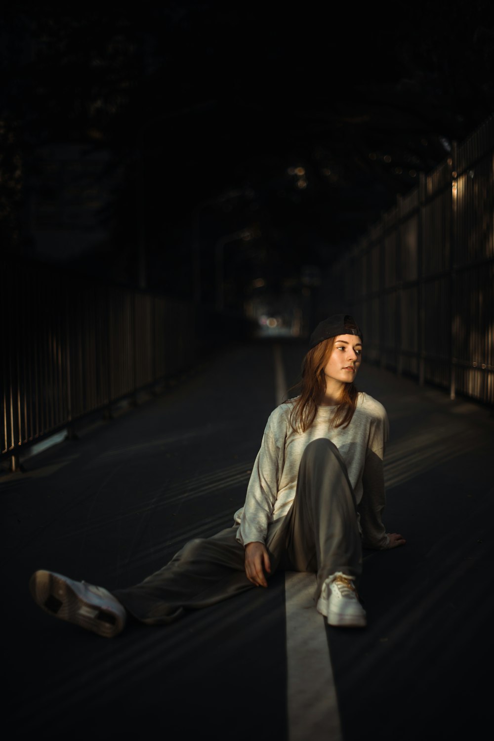 woman in gray coat sitting on the sidewalk during night time