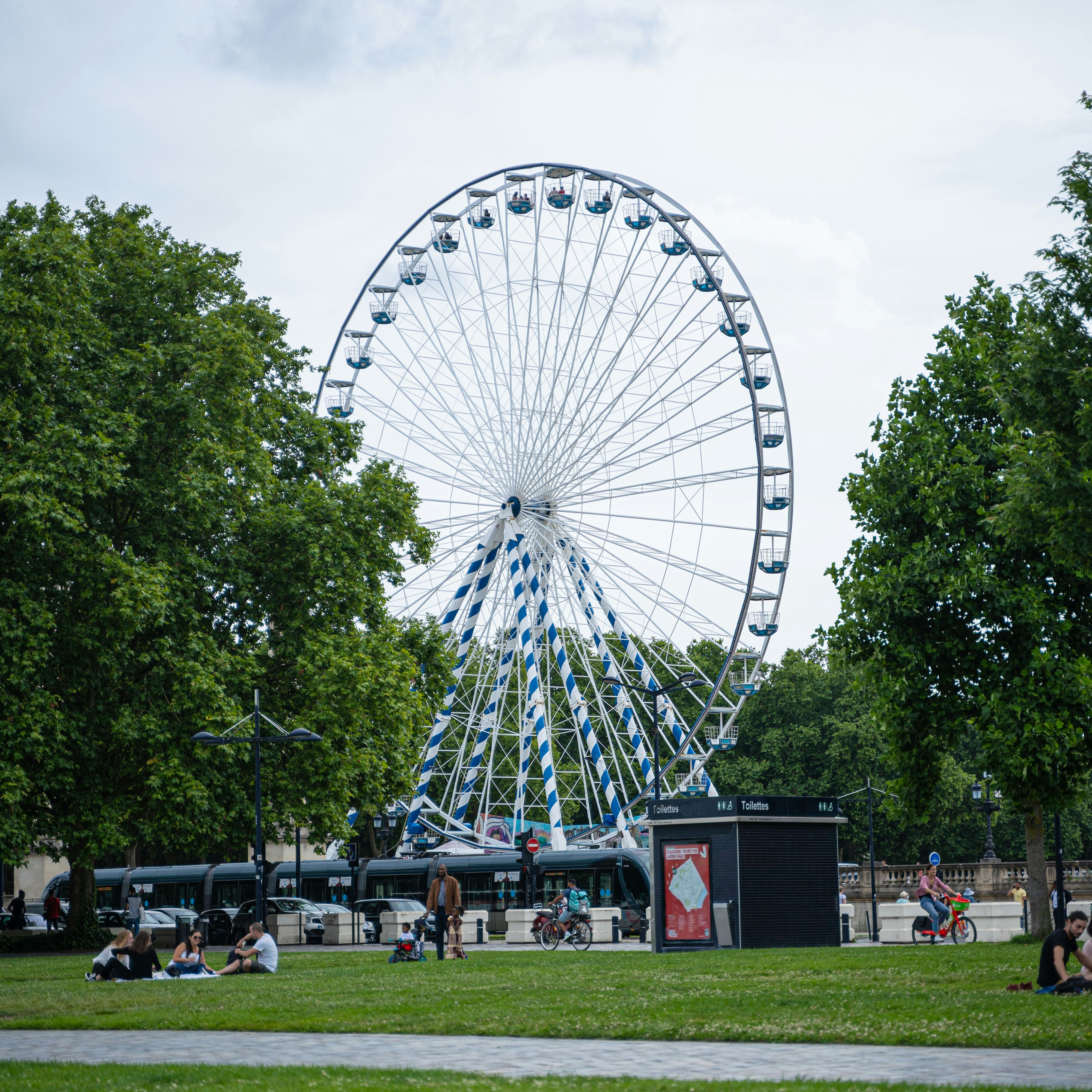 people walking on green grass field near white ferris wheel under white cloudy sky during daytime