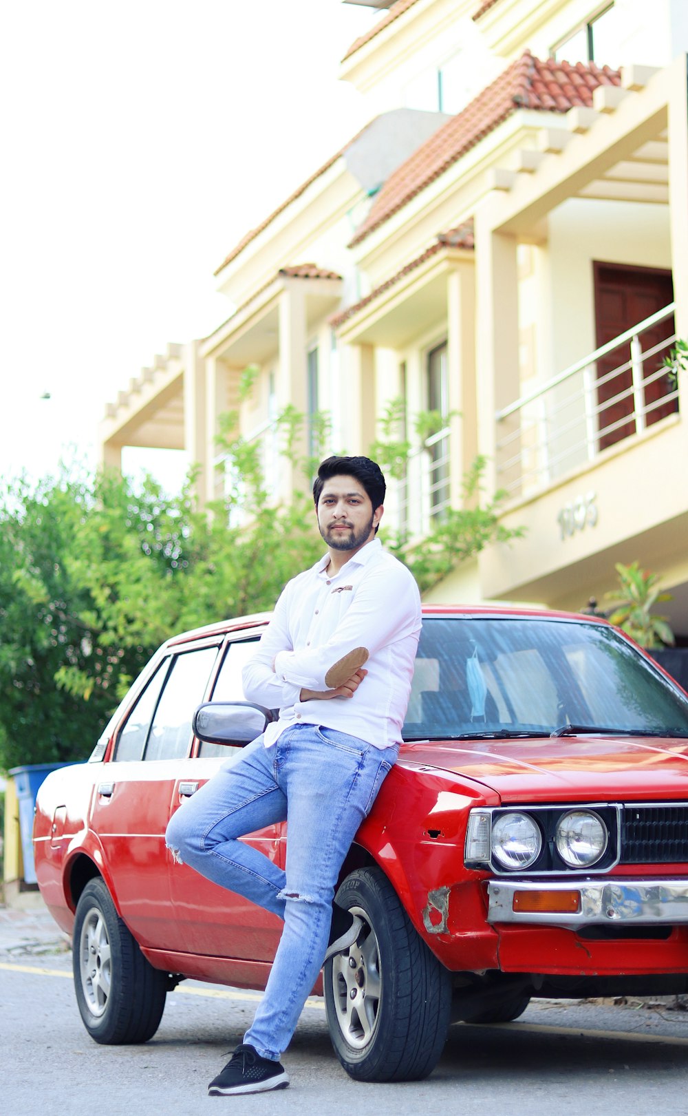 man in white dress shirt and blue denim jeans sitting on red car