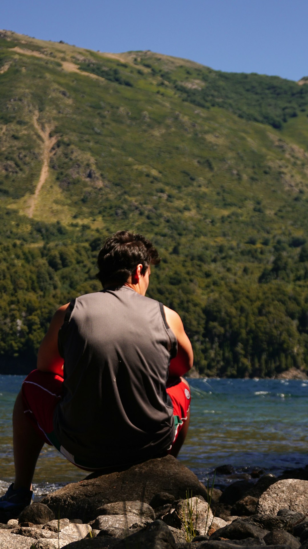 man in gray shirt sitting on red chair looking at the lake during daytime