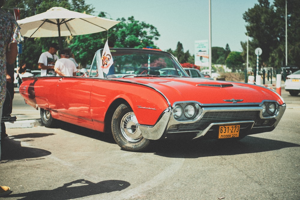 people riding red convertible coupe during daytime