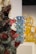 Intricately designed glass sculptures with vibrant colors are displayed on pedestals. The foreground features a dark sculpture with red and translucent spikes. In the background, blue and yellow glass sculptures add contrast and depth.