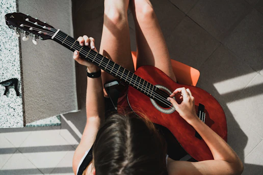 woman in white tank top playing brown acoustic guitar