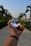 A hand is holding a clear crystal ball that reflects an upside-down image of a path lined with palm trees. The wrist of the hand wears a dark fitness band. The background features a blurred view of more palm trees and a clear blue sky.