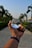 A hand is holding a clear crystal ball that reflects an upside-down image of a path lined with palm trees. The wrist of the hand wears a dark fitness band. The background features a blurred view of more palm trees and a clear blue sky.