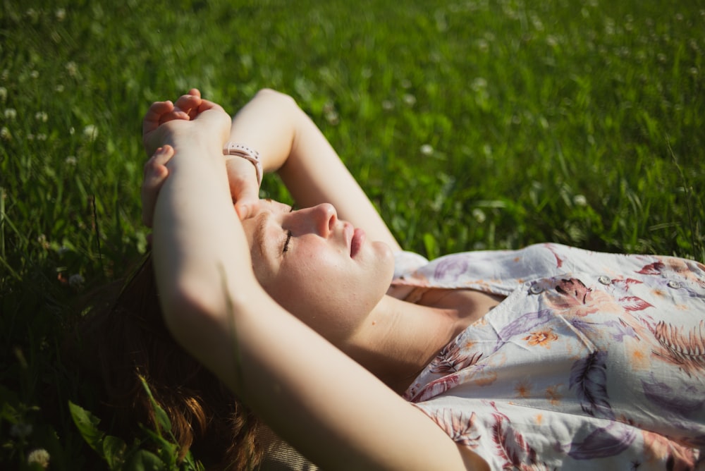 woman in white and blue floral dress lying on green grass field during daytime