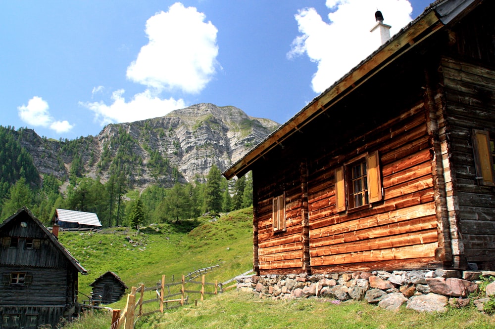 brown wooden house near green grass field and mountain during daytime