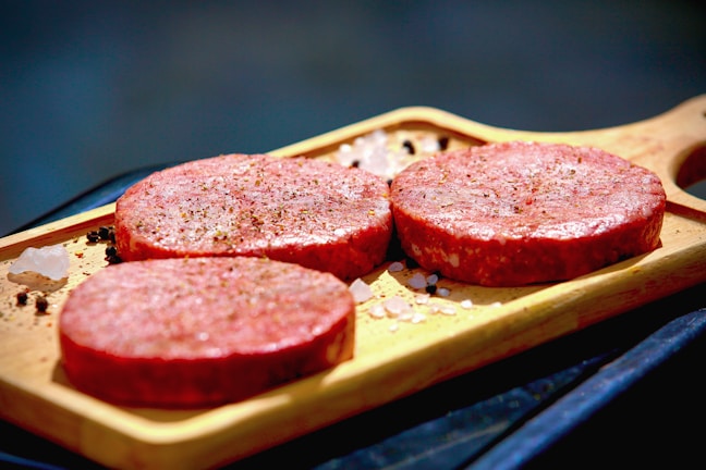 Close-up of fresh Angus beef patties on a wooden cutting board.