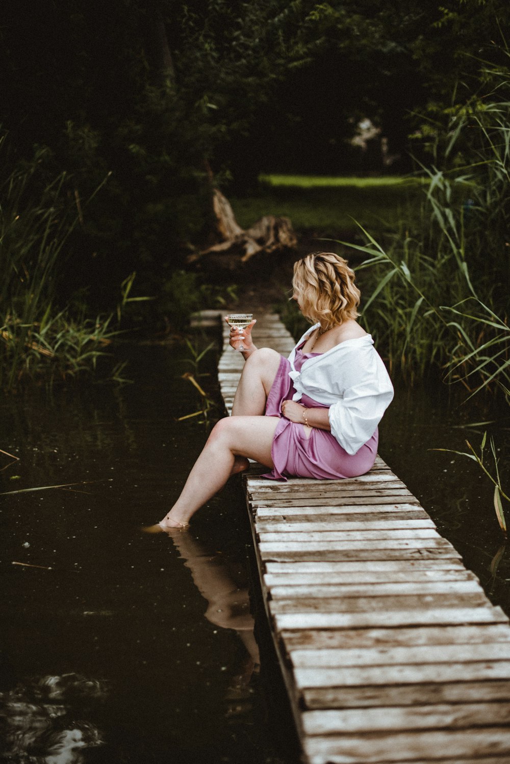 donna in camicia bianca a maniche lunghe seduta sul molo di legno marrone durante il giorno