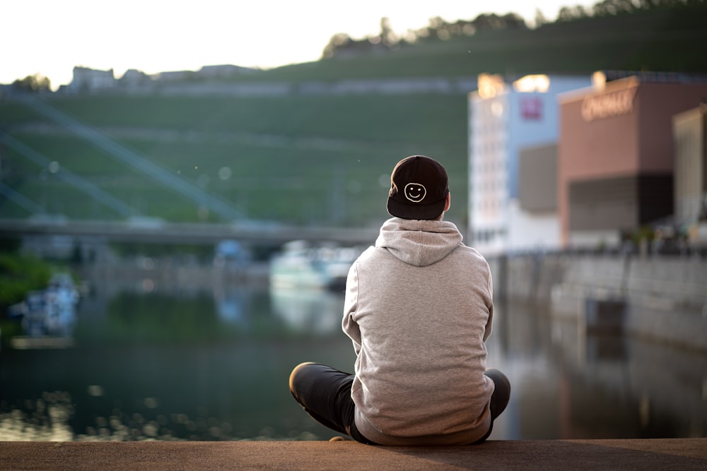 man in gray hoodie sitting on brown concrete surface