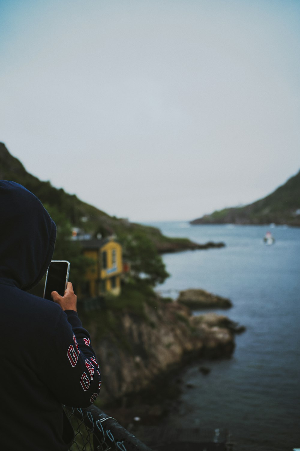 person in black hoodie taking photo of body of water during daytime