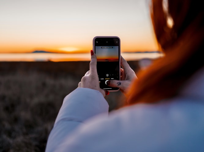 woman holding iphone snapping the sunset