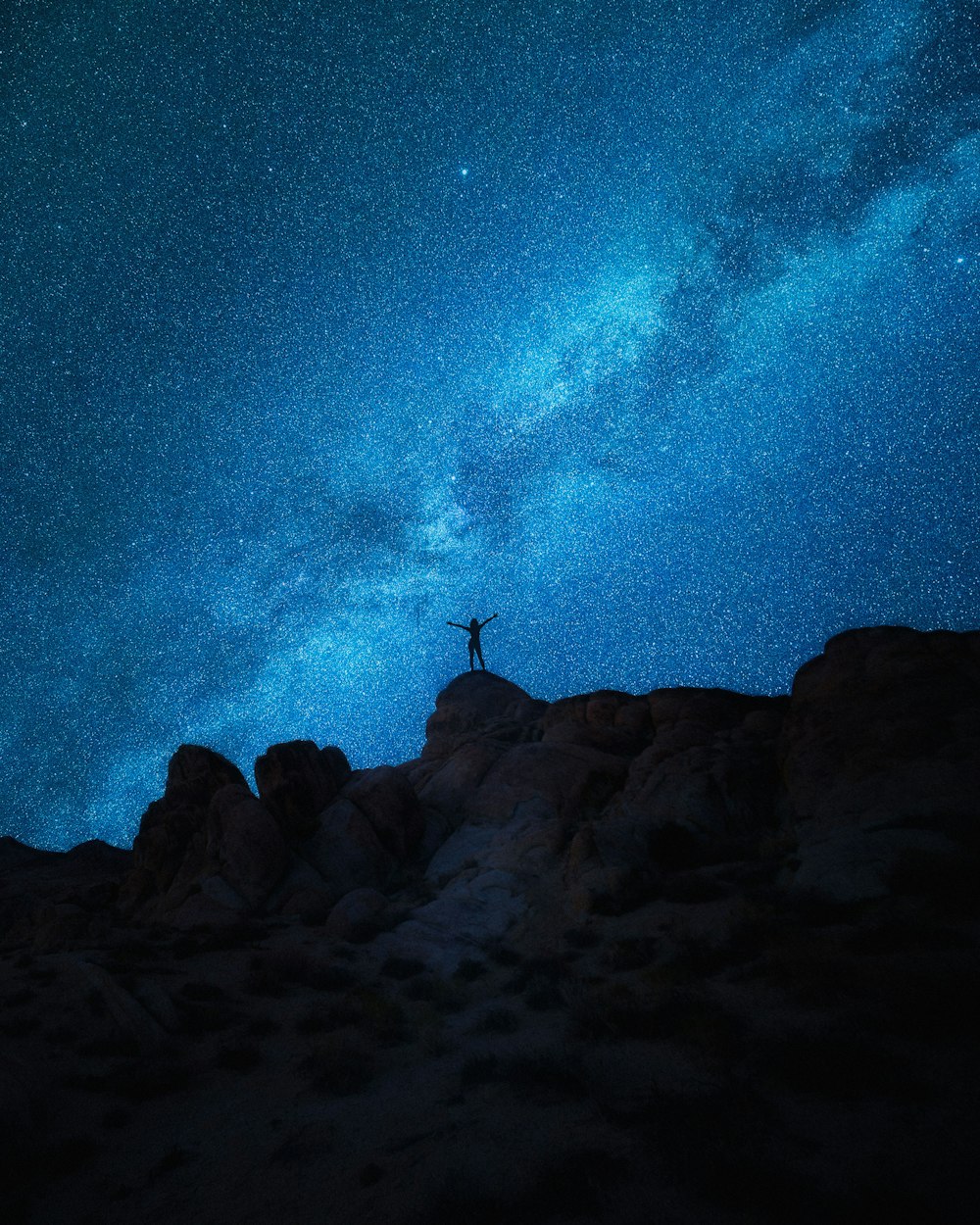 person standing on rock formation under starry night