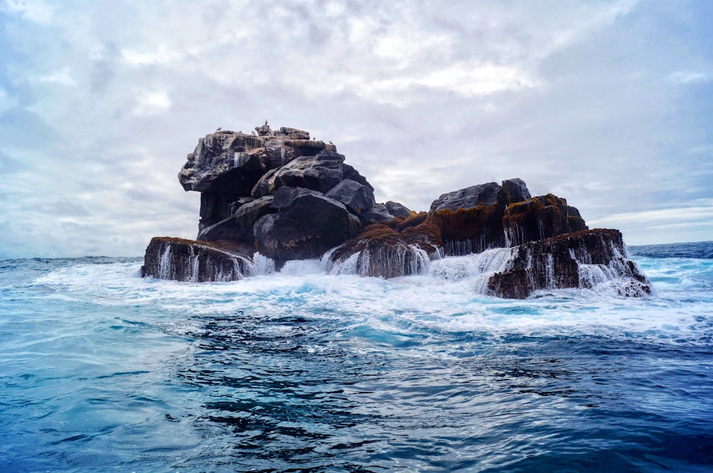 brown rock formation on body of water under white clouds during daytime