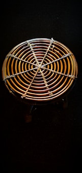 A circular woven object with concentric rings made of rattan or bamboo material is placed against a dark background. It has a sturdy, handcrafted appearance with a detailed weaving pattern evident in the intersecting lines.