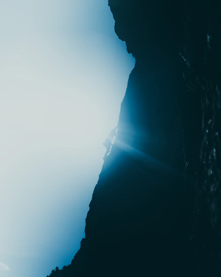 A climber scaling a rugged mountain peak with vibrant morning sunlight casting shadows behind.