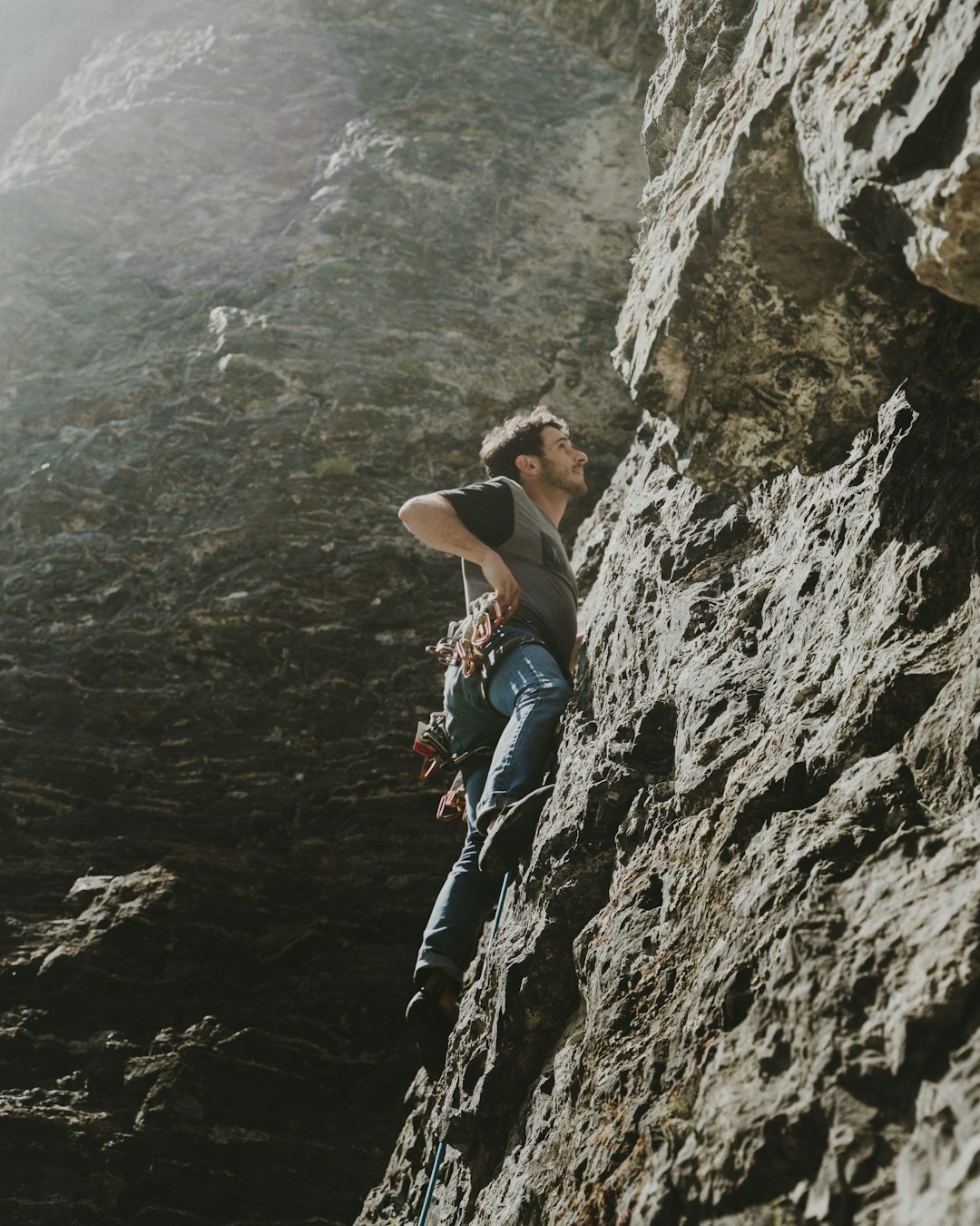 woman in white tank top and blue denim jeans climbing on rocky mountain during daytime