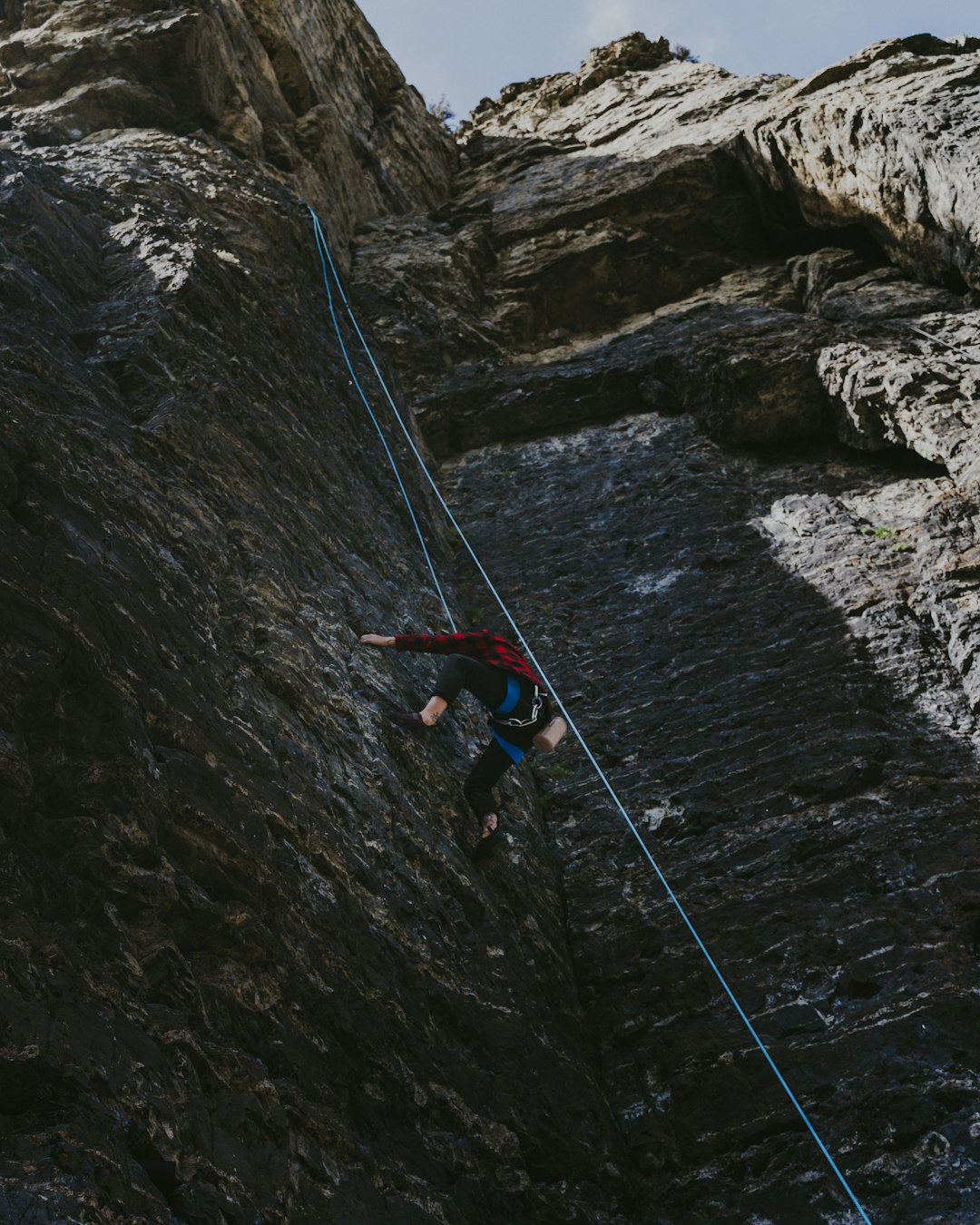 man in red shirt and blue shorts climbing on rocky mountain during daytime