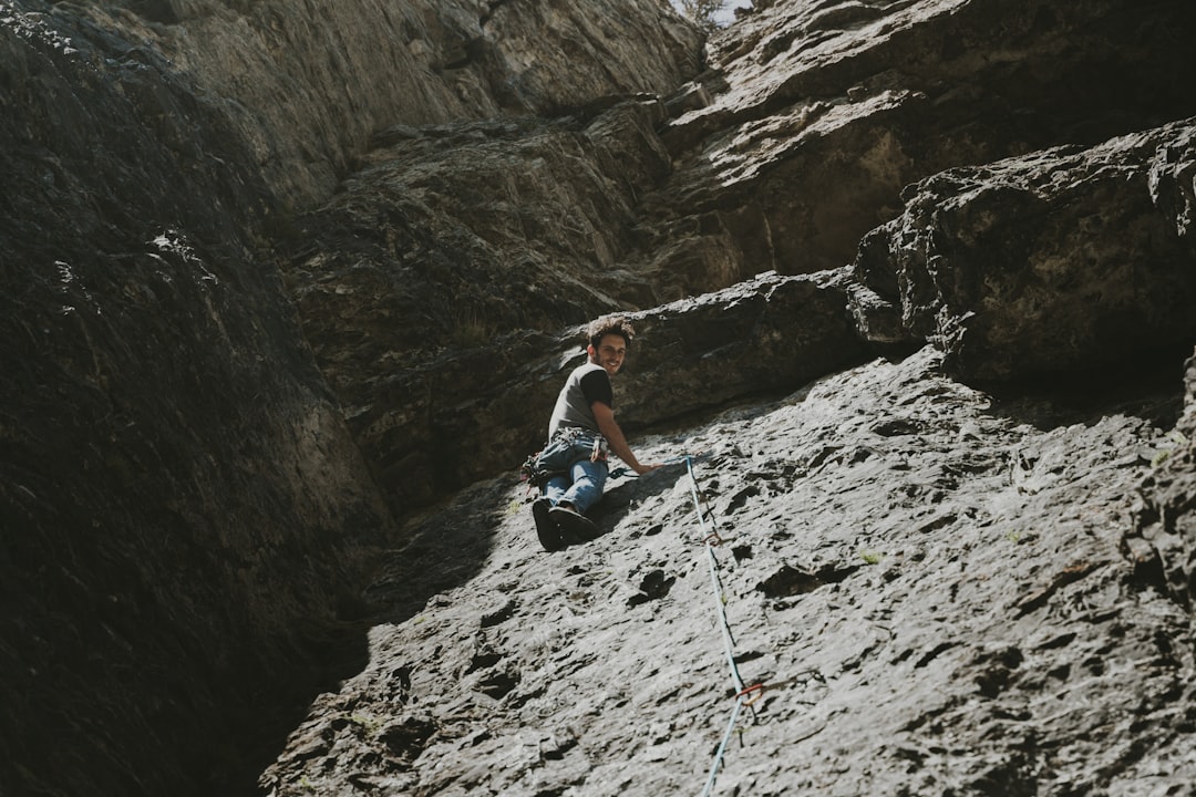 woman in white tank top and black pants sitting on rock mountain during daytime