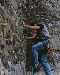 man in black t-shirt and blue denim jeans climbing on gray rock