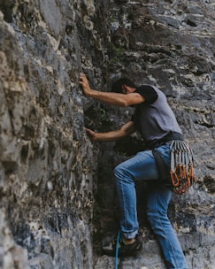 man in black t-shirt and blue denim jeans climbing on gray rock
