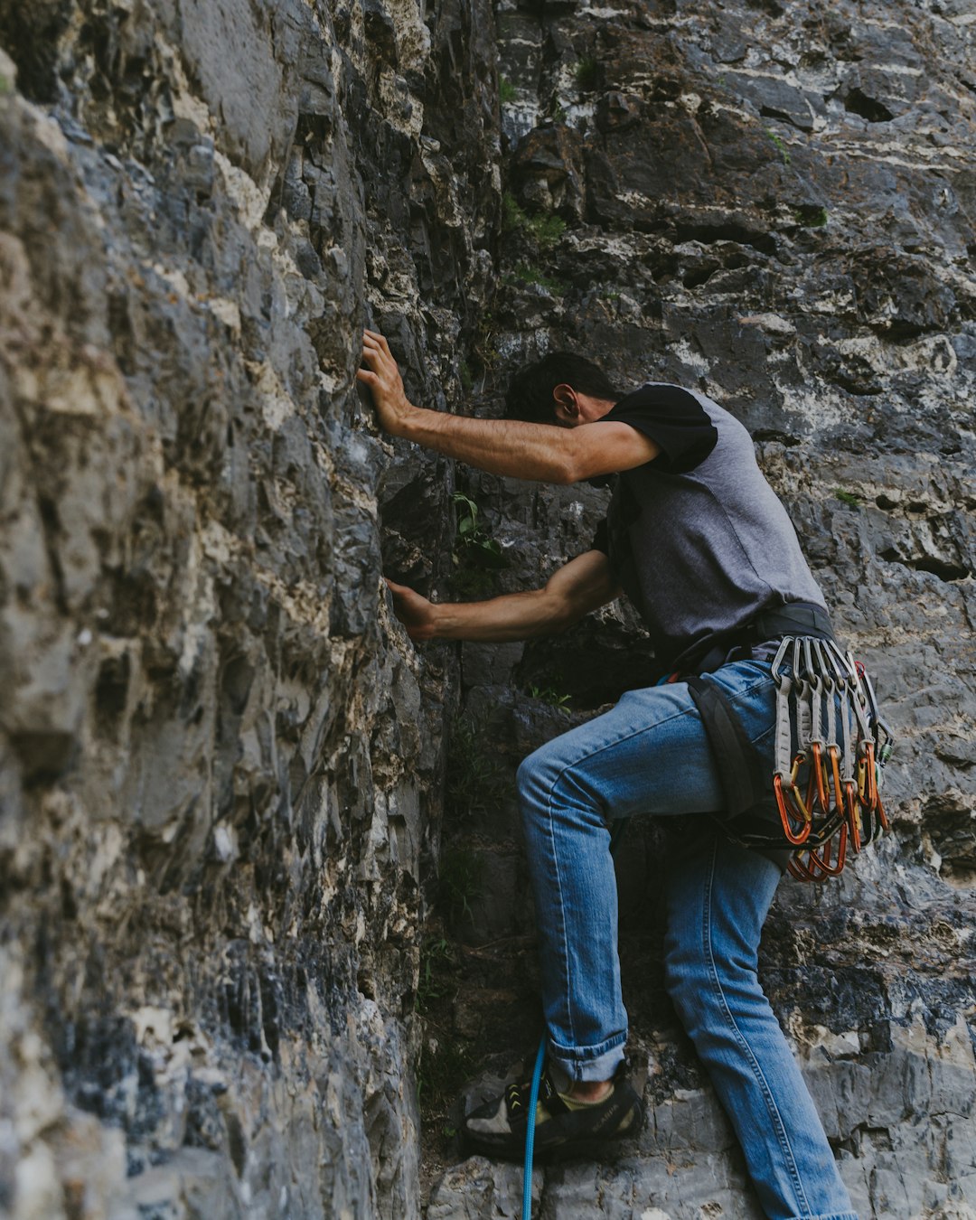 man in black t-shirt and blue denim jeans climbing on gray rock