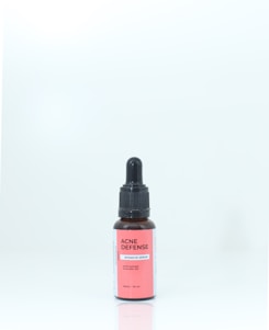 A brown bottle with a black dropper cap, labeled 'ACNE DEFENSE Intensive Serum' on a pink and white label, standing against a plain, light background.