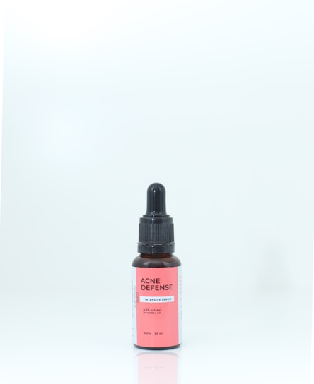 A brown bottle with a black dropper cap, labeled 'ACNE DEFENSE Intensive Serum' on a pink and white label, standing against a plain, light background.
