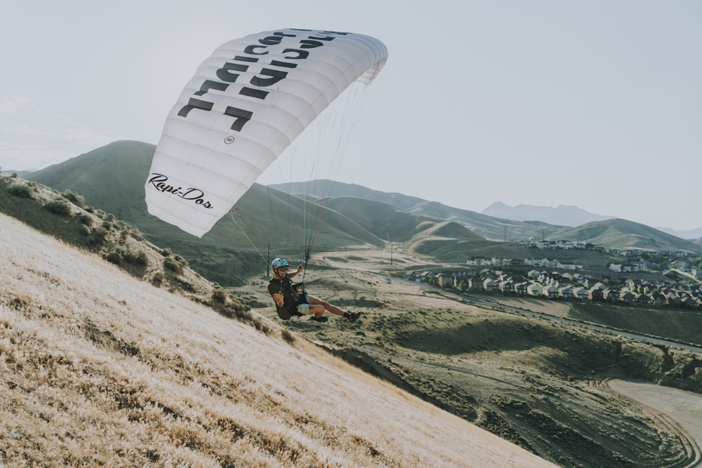 man in green jacket riding on white parachute over green mountains during daytime