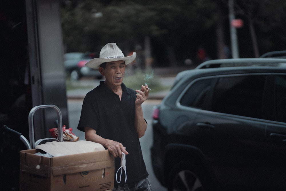 man in black polo shirt and brown hat standing beside black car during daytime