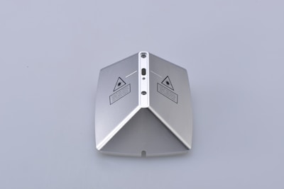 A metallic, pyramid-shaped object with a smooth surface and laser warning labels on two sides. The object has a central ridge with three circular indents and appears to be precision-engineered.