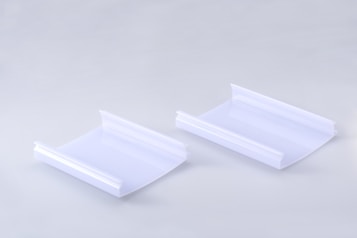 Two identical clear plastic items are positioned side by side on a smooth, light gray surface. Each item has a curved, rectangular shape with raised edges on two opposite sides.
