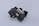 A complex black plastic mechanical component with a beige insert in the center. The piece features various geometric shapes and cutouts, suggesting it might be part of a larger machinery or device.