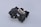A complex black plastic mechanical component with a beige insert in the center. The piece features various geometric shapes and cutouts, suggesting it might be part of a larger machinery or device.