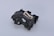 A complex black plastic mechanical component with a beige insert in the center. The piece features various geometric shapes and cutouts, suggesting it might be part of a larger machinery or device.