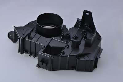 A black plastic automotive component with a circular opening, angular designs, and multiple mounting points.