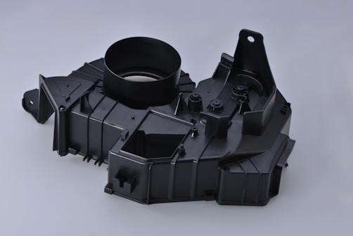 A black plastic automotive component with a circular opening, angular designs, and multiple mounting points.