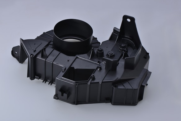 A black plastic automotive component with a circular opening, angular designs, and multiple mounting points.