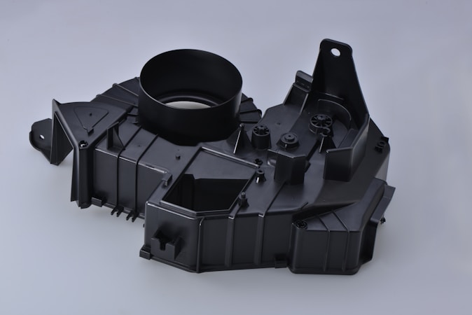 A black plastic automotive component with a circular opening, angular designs, and multiple mounting points.