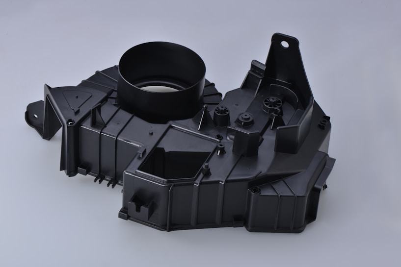 A black plastic automotive component with a circular opening, angular designs, and multiple mounting points.