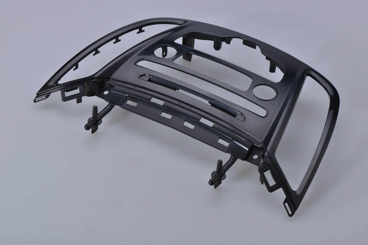 A molded interior trim bezel still carrying its gate stubs
