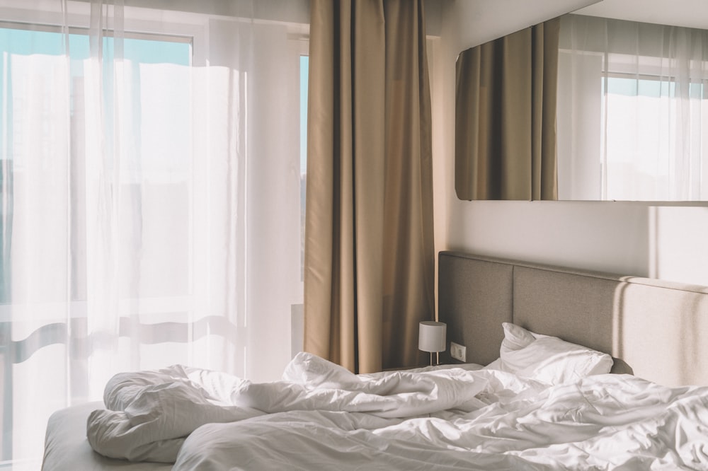 white bed linen near white window curtain