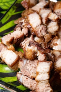 Close-up of sliced roasted pork belly pieces with crispy skin and tender meat, placed on a green leafy patterned surface.