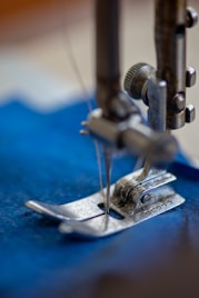 A sewing machine with blue thread in action, crafting a precise seam on a garment.