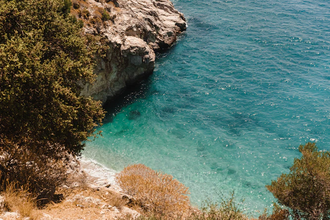 green and brown rocky mountain beside blue sea during daytime