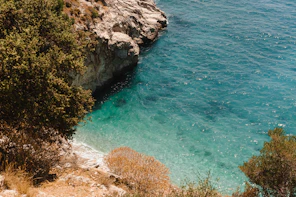 green and brown rocky mountain beside blue sea during daytime
