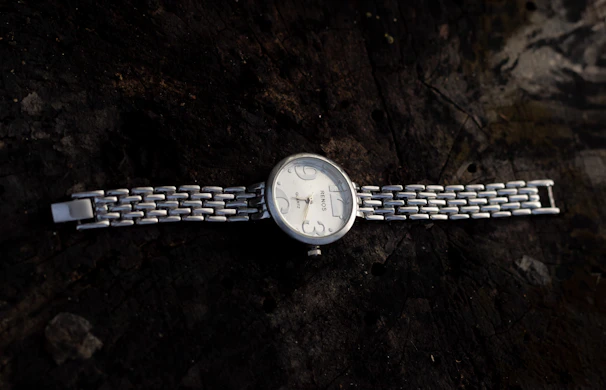 Close-up of a sleek silver watch with a minimalist dial resting on a polished wooden surface.
