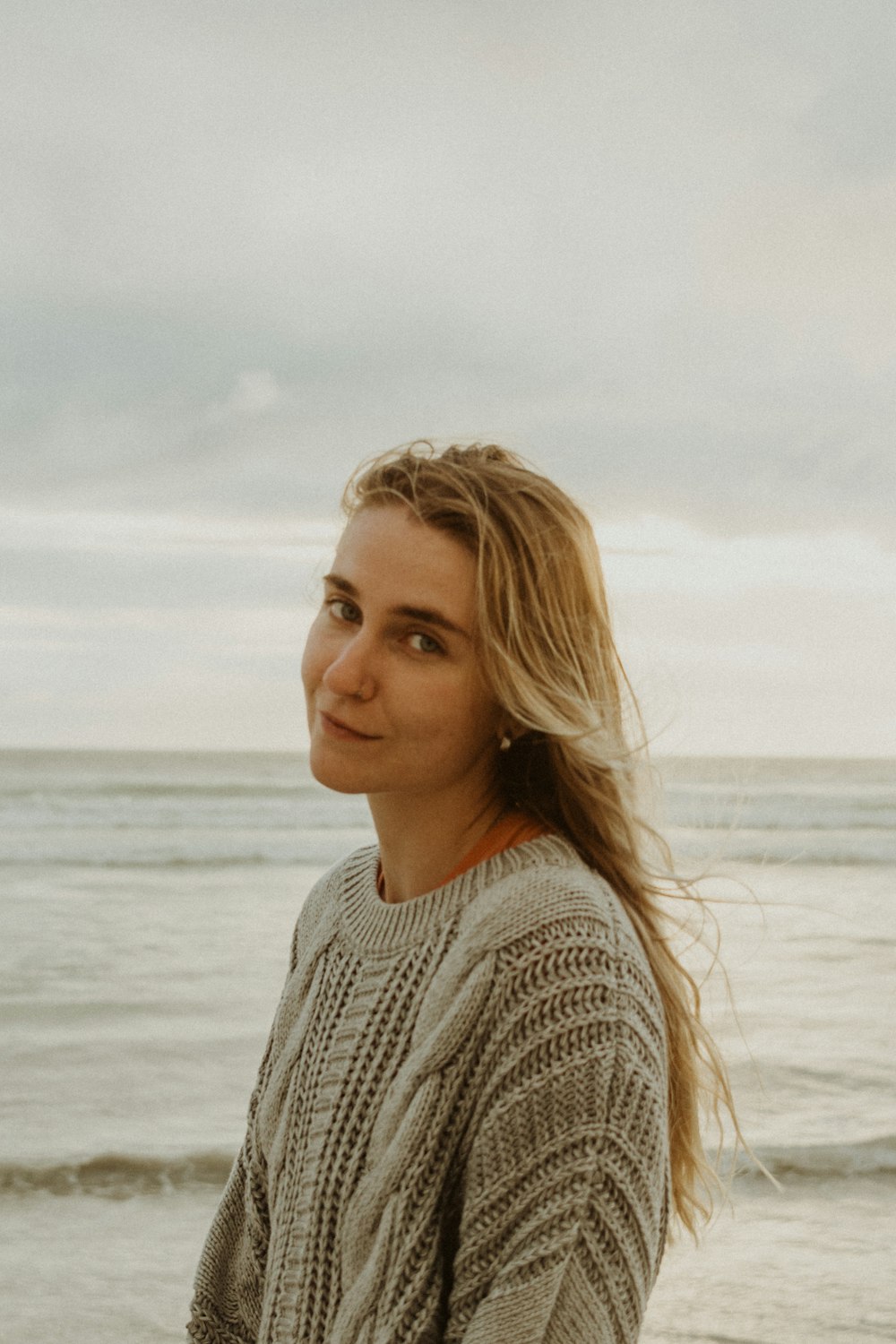 woman in gray knit sweater standing near body of water during daytime