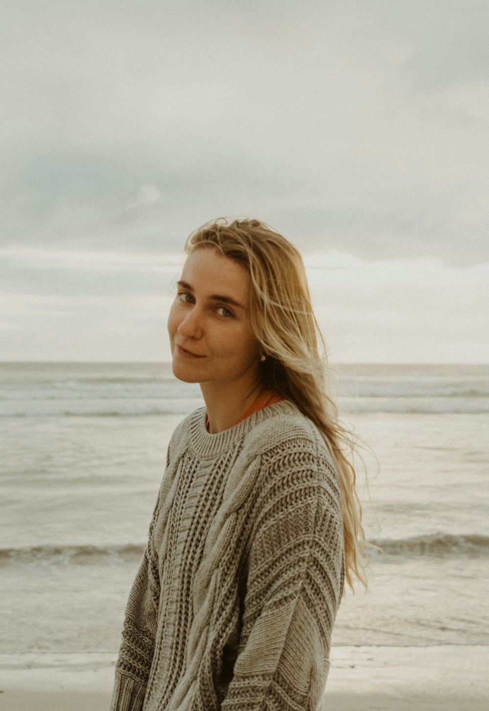 昼間のビーチに立つグレーのニットセーターを着た女性